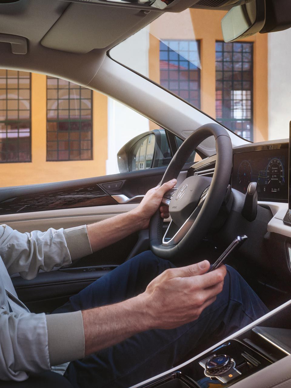 Posnetek notranjosti VW Tiguana. Voznik na voznikovem sedežu s pametnim telefonom upravlja opcijsko aplikacijo VW Connect Plus.