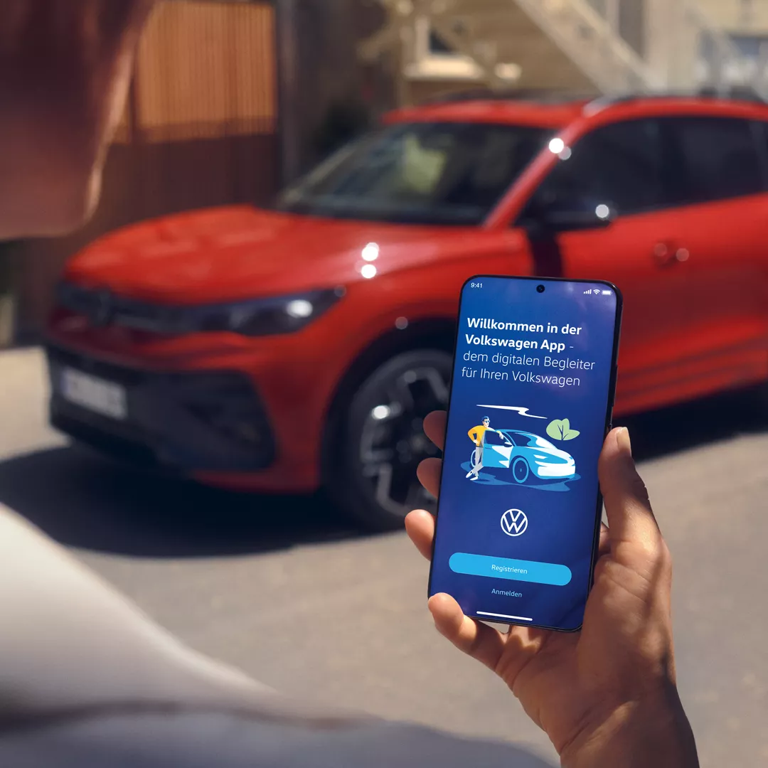 Pogled na zaslon mobilnega telefona s podatki o Tiguanu, v ozadju je parkiran rdeč VW Tiguan.