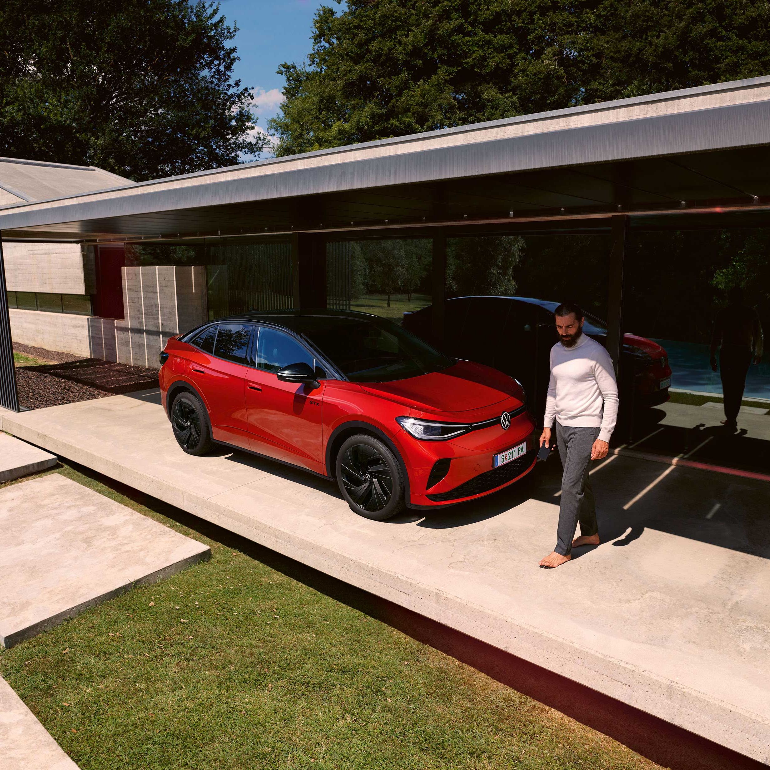 Roter VW ID.5 GTX von schräg vorne in einem modernen Carport, ein Mann geht vor der Motorhaube entlang